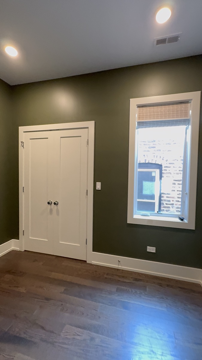 Before painting: dark green bedroom walls with white closet doors and window trim in Chicago.