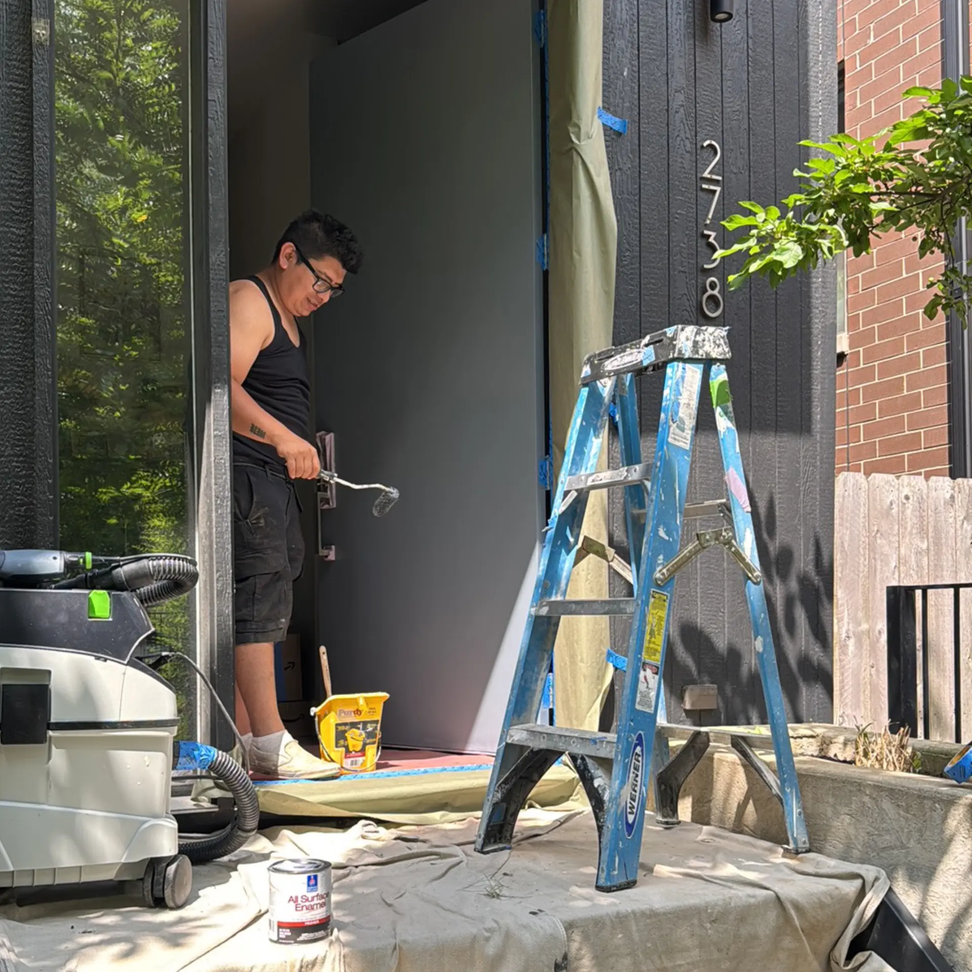 Painter working beside dark exterior siding and a ladder